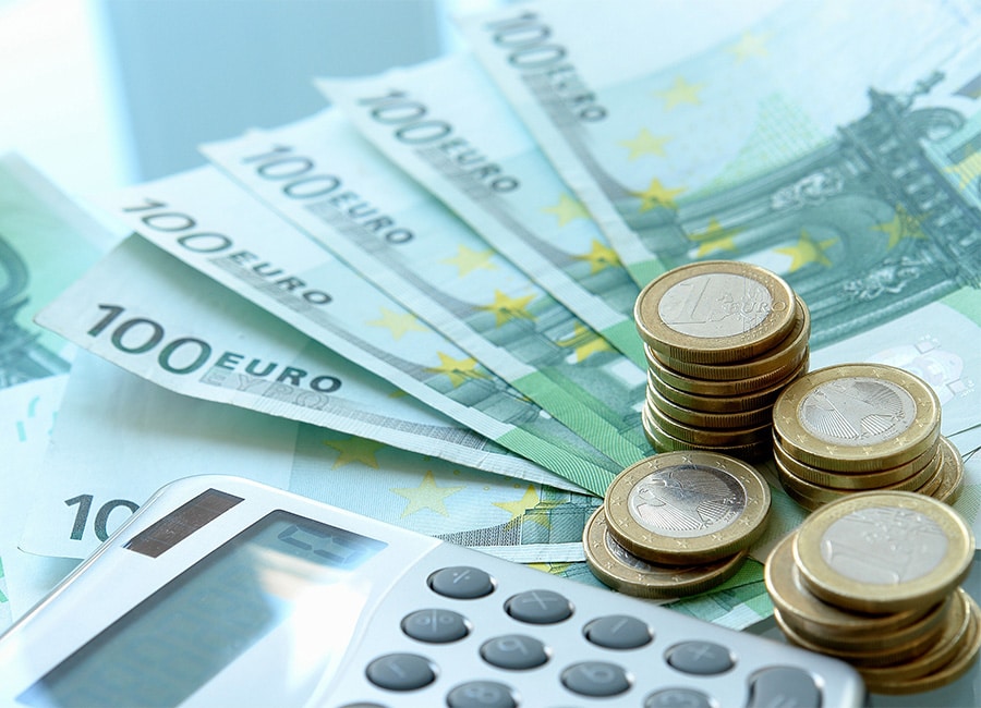 Euro banknotes and coins beside a calculator on a light background.
