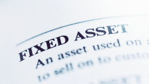 Close-up of a printed page with the heading "FIXED ASSET" in bold, highlighting how business basics and key business principles are explained for entrepreneurs, with partially visible descriptive text below.