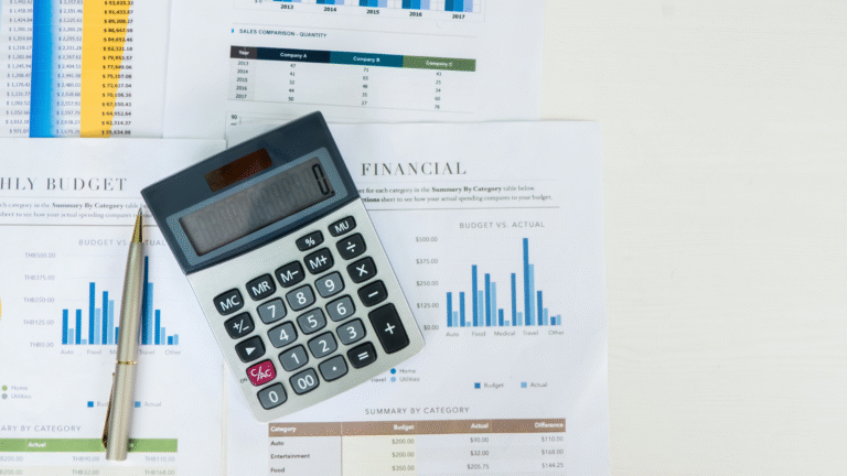 A calculator and pen rest on financial documents displaying charts, tables, and budget summaries on a white desk.