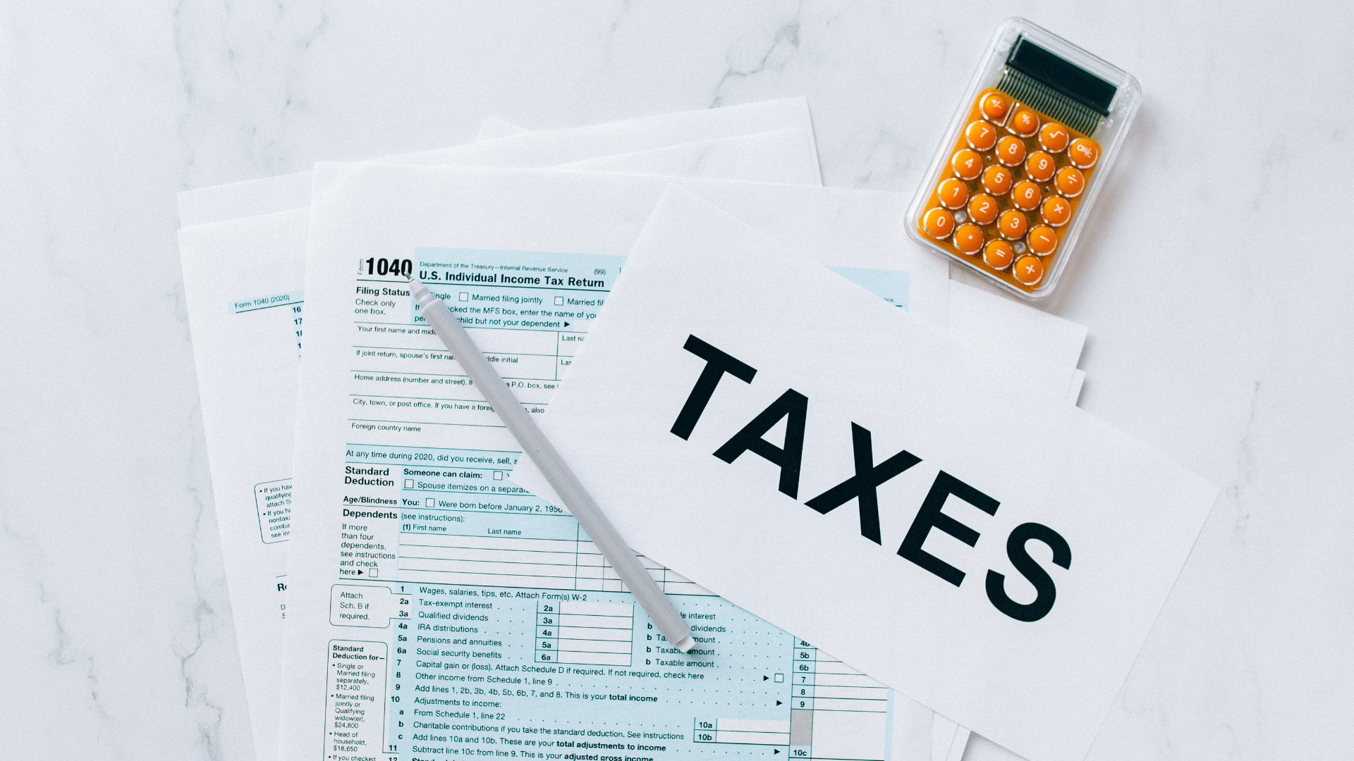 A stack of tax forms, a pen, and a calculator are arranged on a white surface, with a paper labeled "TAXES" on top—perfect for tackling your tax preparation checklist this tax season.